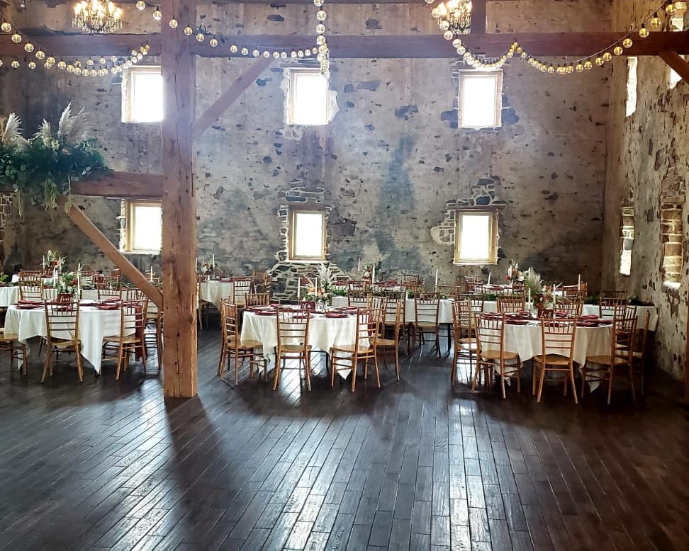 Sunlit stone barn set for a seated dinner with white linens and gold chiavari chairs