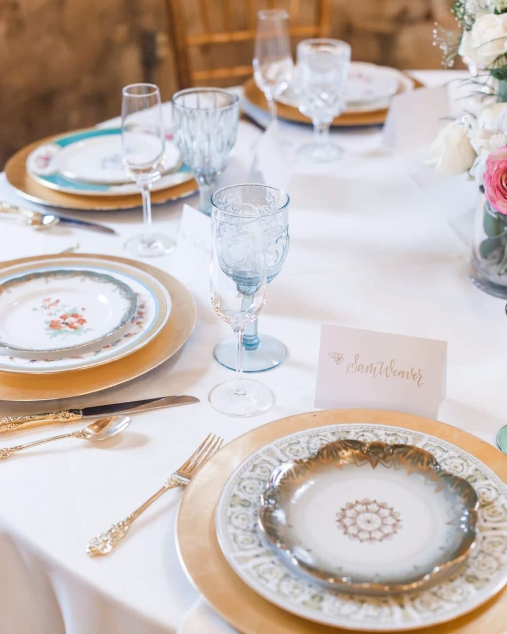 Place setting with a gold charger, vintage china, blue glassware and a calligraphy place card