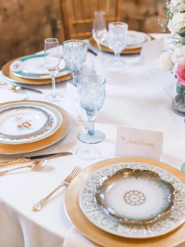 Place setting with a gold charger, vintage china, blue glassware and a calligraphy place card
