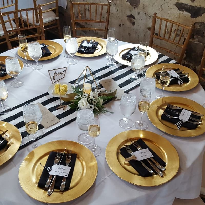 Round tables set with gold chargers and black napkins for a gala dinner