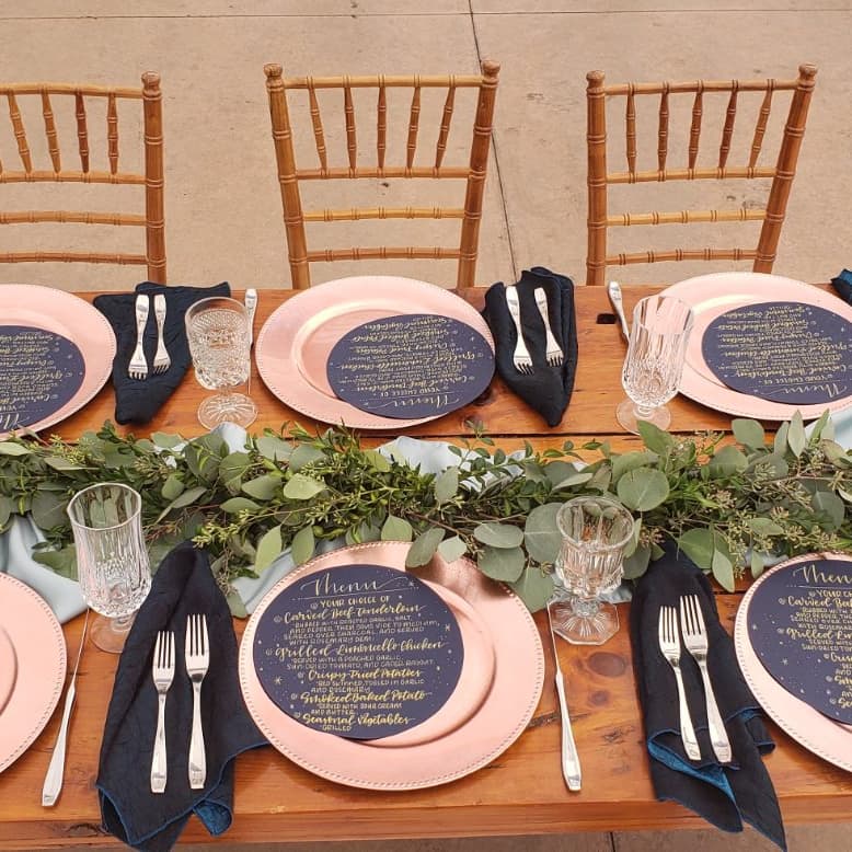 Place settings with patterned plates, navy napkins and a greenery runner on a wooden table