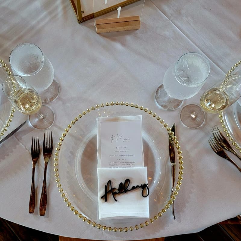 Glass charger plate and gold flatware on white linen seen from above