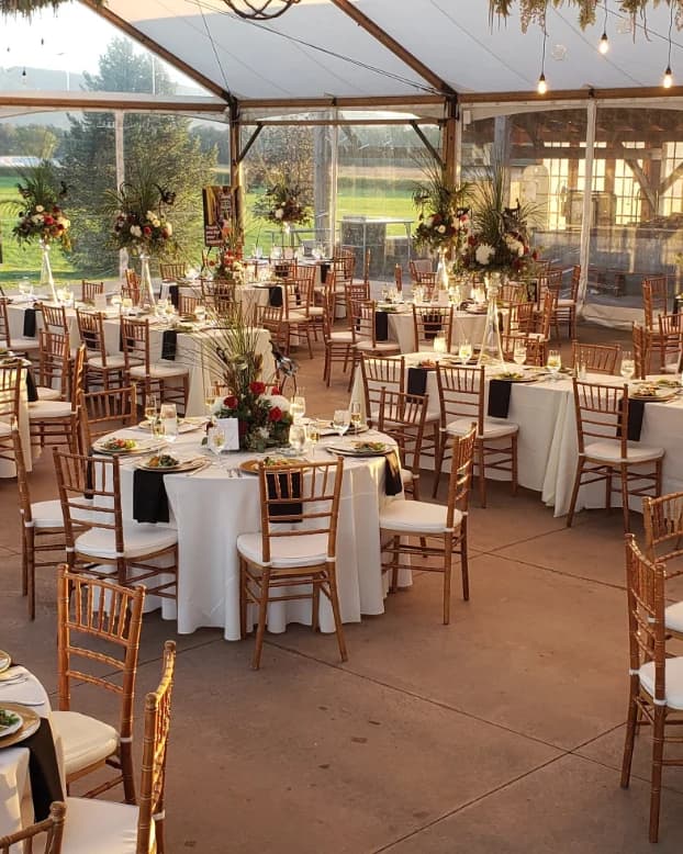 Tented wedding reception with round tables, gold chiavari chairs and tall floral arrangements at dusk